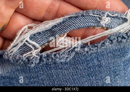 jeans strappati dall'usura a lungo termine, parte di jeans blu realizzati in tessuto di cotone sfrangiato e strappato dall'usura e dall'uso a lungo termine Foto Stock