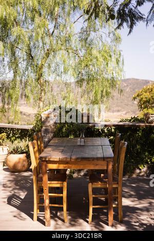 Tradizionale taverna greca tavolo da pranzo all'aperto con sedie in legno sotto l'albero di salice, Creta Grecia. Posti a sedere rustici all'aperto con vista sulle montagne. Foto Stock