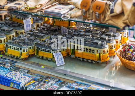 Dettagliati souvenir in tram in metallo vintage su uno scaffale di vetro in un negozio di articoli da regalo a Lisbona, Portogallo, con prodotti tradizionali in sughero sullo sfondo. Foto Stock