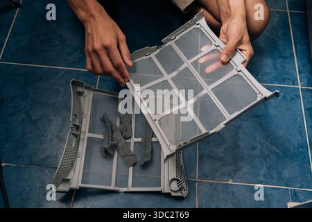 Vista ad angolo alto dell'uomo che pulisce i residui accumulati dal filtro dell'essiccatore, dimostrando la routine di lavoro domestico e la manutenzione essenziale dell'apparecchio per Foto Stock
