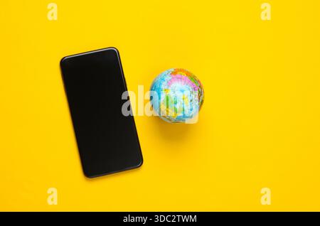 Smartphone e globo su sfondo giallo. Rete globale. Comunicazioni mobili in tutto il pianeta. Rete globale 5G. Foto Stock
