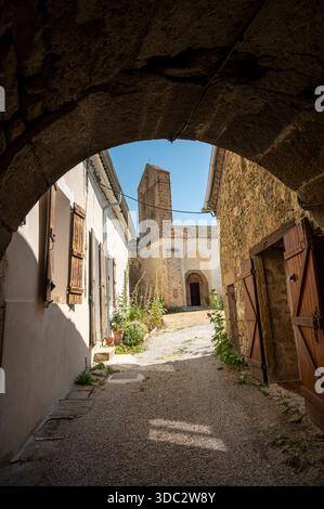 Prieuré de Saint-André-de-Rosans incorniciato da una porta ad arco in pietra sotto un cielo estivo azzurro, che mette in risalto l'architettura storica del monastero Foto Stock