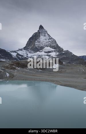 Vista aerea dell'iconica vetta del Cervino che pierta il cielo, riflessa nel tranquillo lago turchese sottostante, Trockener Steg, Vallese, Svizzera. Foto Stock