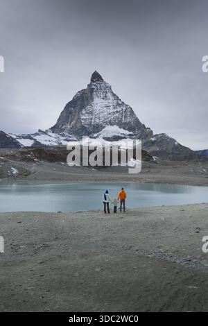 Vista aerea dell'iconica vetta del Cervino maestosamente sopra un lago glaciale, con i suoi pendii polverati di neve che contrastano con il terreno roccioso aspro, Z Foto Stock