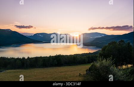Tramonto sul lago. La scena mostra i monti Blåhøa e Gjevilvasskamben nella catena del Trollheimen a Oppdal in Norvegia. La luce serale si riflette sull'acqua Foto Stock