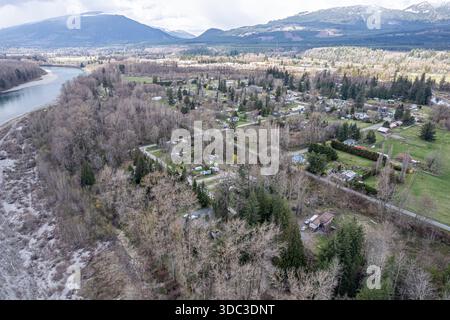 Vista aerea di un fiume che serpeggia davanti a una piccola città annidata tra gli alberi, con montagne che si innalzano in lontananza, Hamilton, Washington, Stati Uniti. Foto Stock