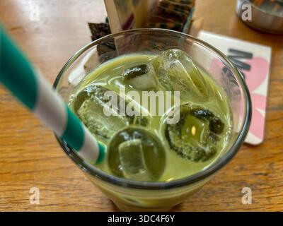 Vista dall'alto del tè matcha freddo con cubetti di ghiaccio trasparente in un bicchiere, servito su un tavolo di legno. Bevanda rinfrescante a base di tè verde con cannuccia, perfetta per l'estate. Foto Stock
