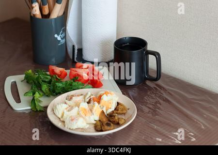 Natura morta quotidiana di uova sode, funghi saltati, pomodori freschi, verdure, tazze, utensili sul tavolo di casa Foto Stock