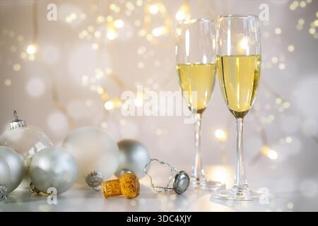 Due flute di champagne, baubles di Natale e il sughero su uno sfondo caldo e leggero con luci fiabesche e bollicine bokeh, feste natalizie l Foto Stock