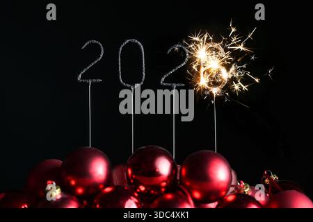 Scintille bruciate a forma di anno 2026, ma il 6 è ancora bruciato e spruzza scintille, baule natalizie rosse, sfondo nero, concetto per ne Foto Stock