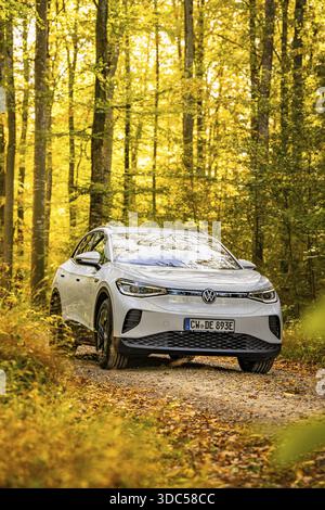 In autunno un SUV percorre un sentiero forestale circondato da foglie gialle sotto la luce del sole, auto elettrica VW ID4, condivisione di auto con cervi, Calw, Germania Foto Stock