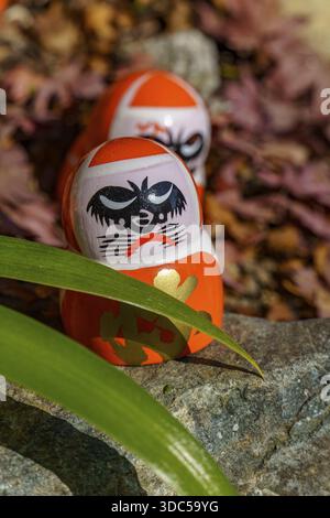 Primo piano di bambole Daruma con dettagli circondati da foglie e pietre, Osaka, Giappone Foto Stock