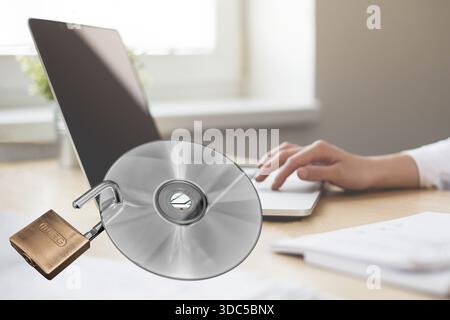 Scrivania da ufficio con laptop vicino alla finestra, mani e dita che toccano il laptop, immagine di sfondo con immagine in primo piano, CD dati con blocco a U aperto, IT e O. Foto Stock