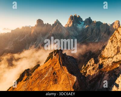 Suggestivo paesaggio alpino di alba dorata che risplende su Cadini di Misurina con aspre cime montane e la crescente nebbia nelle Dolomiti, Italia Foto Stock
