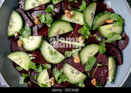 Insalata vegana di barbabietole. Barbabietola a fette marinata con cetriolo fresco, noci e foglie di coriandolo in un recipiente di ceramica. Background alimentare. Sano, a base vegetale Foto Stock