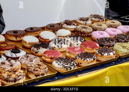 Varietà di ciambelle fresche con diversi condimenti, tra cui spolverini di cioccolato glassa alla vaniglia glassa rosa disposte su vassoio dorato Pasticceria dolce Foto Stock