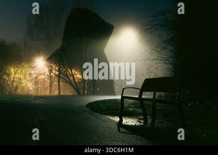 Un fantasma come una persona incappucciata in un parco in una tranquilla notte di inverni nebbiosi in un parco Foto Stock