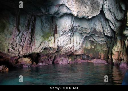 All'interno di una grotta costiera sul mare con pareti di roccia a strati e colorate texture minerali riflesse nelle calme acque turchesi lungo la costa mediterranea Foto Stock