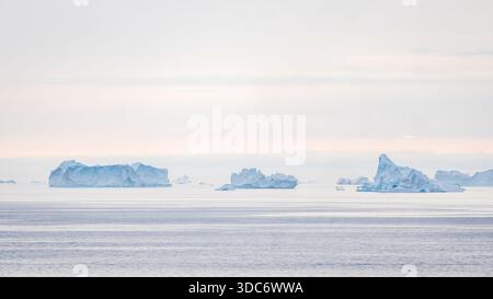 Tre iceberg distanti che fluttuano sotto il cielo artico nuvoloso Foto Stock