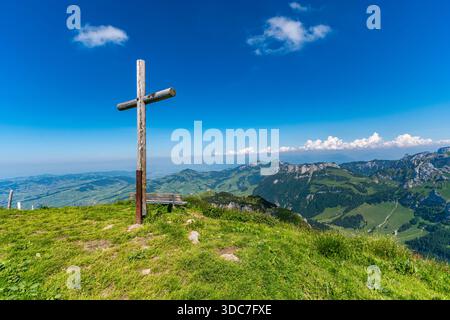 Una croce di legno intemprata si erge su una lussureggiante vetta di montagna verde, evocando pace e riflessi su paesaggi alpini mozzafiato e blu senza fine Foto Stock
