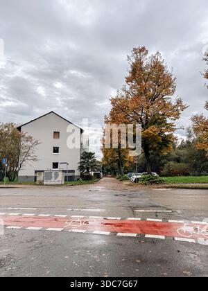 Rastatt, Germania - 15 ottobre 2024: Una pittoresca scena autunnale mostra un edificio residenziale accanto a alberi colorati che costeggiano una strada tranquilla con un Foto Stock