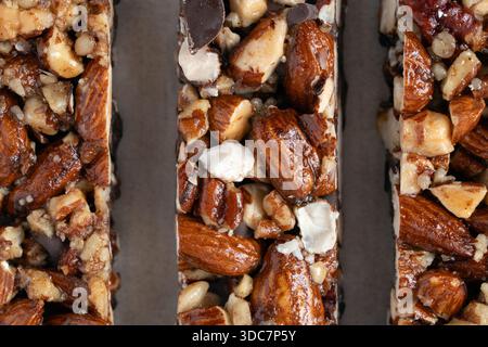 Foto macro dettagliata che mette in evidenza la ricca consistenza di tre barrette di noci e cioccolato, con mandorle intere e tritate, perfetta per uno spuntino sano Foto Stock
