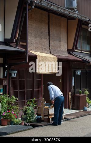 L'uomo beve dall'acqua sorgiva a due livelli "mizubune" (水舟) acqua di legno per bere, lavare e raffreddare cibo, Gujo-Hachiman (郡上八幡) a Gifu, Giappone. Foto Stock