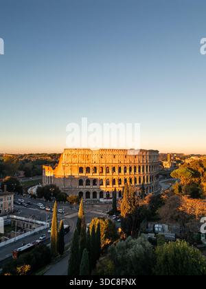 Veduta aerea del Colosseo, un antico anfiteatro romano e iconico monumento, si erge illuminato dalla luce dorata dell'alba, a simboleggiare il turismo Foto Stock