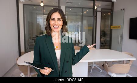 Giovane donna professionale felice che punta la mano verso gli interni moderni dell'ufficio Foto Stock