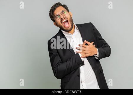 Stressato uomo d'affari indiano spaventato soffre di tensione che tiene il petto con attacco di dolore cardiaco rischio di ictus sintomo di pressione, sentirsi male malato. Uomo arabo maschio ragazzo isolato su sfondo grigio Foto Stock