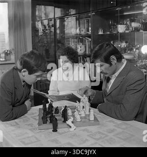 Slaviansk, RSS Ucraina, URSS - 1981: Fotografia di stile di vita d'archivio che cattura una serata di famiglia sovietica. Un padre con i baffi gioca a scacchi con suo figlio a un tavolo, mentre la madre legge una rivista sullo sfondo. La camera presenta un tipico interno tardo sovietico, che include un'unità a parete lucida ("stenka") piena di cristallo e libri. Questa scena riflette la popolarità degli scacchi e la stabilità interna nella pacifica regione del Donbass durante la fine dell'era sovietica. Foto Stock