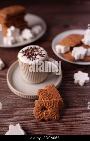 ambiente accogliente con cappuccino e biscotti sul tavolo di legno, con latte art con spruzzette di cioccolato e biscotti decorativi completati da bianco Foto Stock