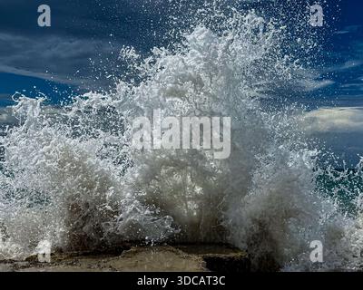 La potente onda oceanica che si schianta contro la costa rocciosa, il movimento ghiacciato di acqua bianca si tuffa sotto un cielo azzurro. Foto Stock