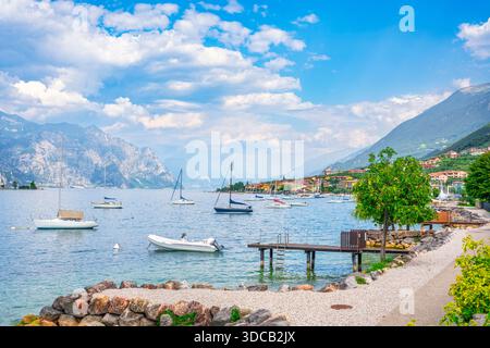 Vista panoramica sul lago delle barche a vela ormeggiate e una pista ciclabile sul lungomare a Malcesine, in Veneto. Paesaggio estivo sul Lago di Garda, Italia Foto Stock