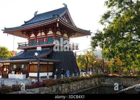 Uno storico complesso di templi giapponesi caratterizzato da una pagoda a più livelli, strutture di legno scuro e un luminoso tetto visitatori curiosano in un negozio e passeggiano per Foto Stock