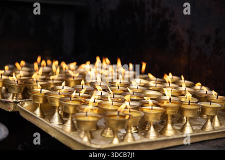 File di lampade a burro tradizionali che bruciano su un vassoio metallico in Nepal. Una calda luce di candela crea una tranquilla e suggestiva scena di natura morta. Foto Stock