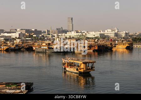 Crociera in dhow al tramonto lungo il porto di Doha Corniche, con barche tradizionali e vista dello skyline Foto Stock