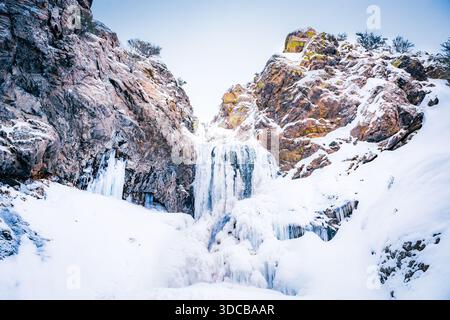 Cascata ghiacciata circondata da scogliere innevate nel paesaggio invernale dello Utah. Foto Stock