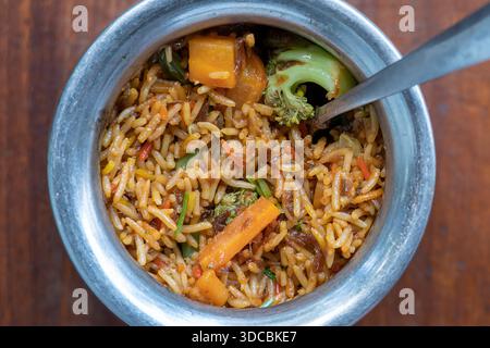 Biryani allo zafferano Navratico con verdure fresche, spezie e riso basmati in una pentola di metallo su sfondo di legno, vista dall'alto, primo piano. Cucina indiana Foto Stock