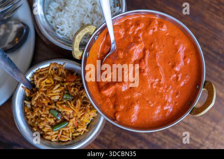 Biryani allo zafferano Navratico con verdure fresche, spezie e riso basmati in una pentola metallica e pezzi di pollo in salsa al curry rosso su fondo di legno, Foto Stock