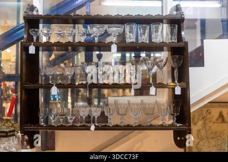 Londra, Regno Unito, 2 dicembre 2025, scaffale a parete in legno che espone vari bicchieri da vino e calici antichi in cristallo. Foto Stock