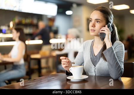 Giovane donna con il telefono in mano in un bar Foto Stock