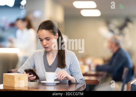 Giovane donna con il telefono in mano in un bar Foto Stock
