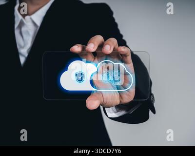 Uomo d'affari che possiede un futuristico telefono in vetro con simbolo di sicurezza del cloud e icone di elaborazione dati sullo schermo, che rappresenta il cloud computing e la cybersicurezza Foto Stock