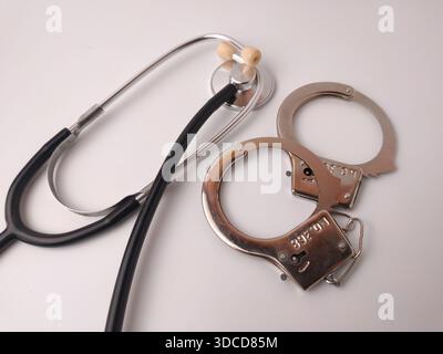 L'immagine mostra uno stetoscopio e un paio di polsini in metallo, comunemente usati per simboleggiare l'abuso medico. Foto Stock