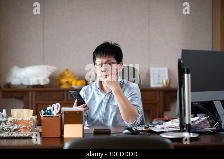 uomo d'affari asiatico che usa lo smartphone in ufficio Foto Stock