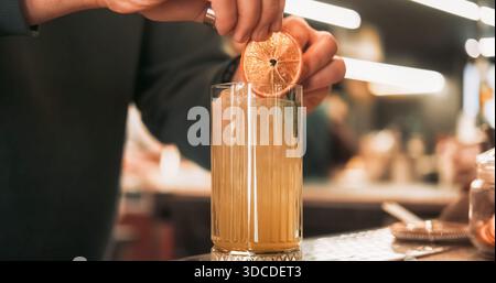 Bevanda per guarnire. Ricetta per cocktail. Il barista aggiunge una fetta di agrumi essiccati alla bevanda rinfrescante. Succo d'arancia aromatico miscela alcolica. Foto Stock