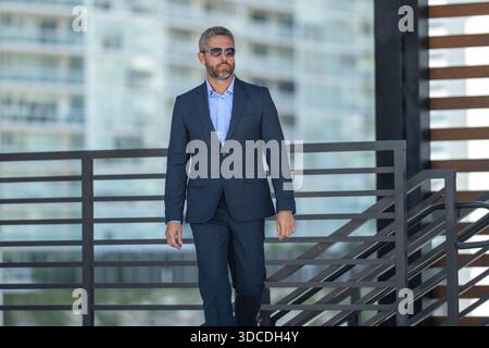Uomo d'affari di successo che cammina all'aperto. Uomo d'affari sicuro di sé. Business di successo. Uomo d'affari maturo in tuta. Bel leader aziendale. Ricco Foto Stock
