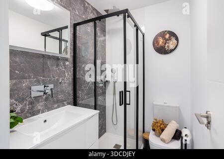 Bagno moderno con doccia in vetro, piastrelle in marmo, lavandino bianco ed eleganti elementi decorativi Foto Stock