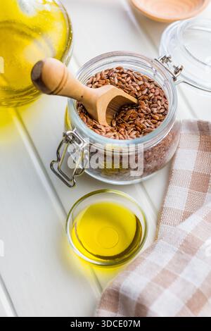 Semi di lino o semi di lino e olio. Semi sani di lino in vaso su un tavolo bianco. Foto Stock